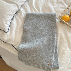 Detail of gray knitted scarf with soft fuzzy texture and gold ring charm on white linen