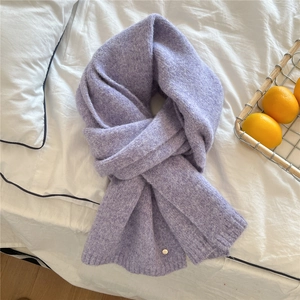Close-up of soft purple knit scarf with a small metal tag on white bedding