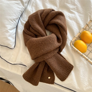 Detailed texture of thick dark brown knitted scarf on white bedding with decorative basket
