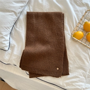 Detail of dark brown knit scarf with gold metal emblem on soft white bedding