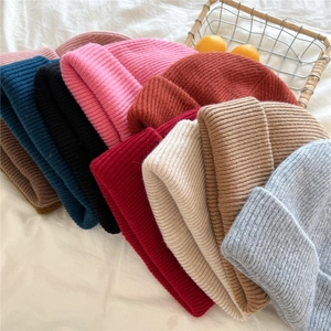 Close-up of various ribbed knit beanie colors including pink, beige, and camel stacked neatly