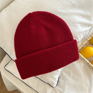 Detailed knit texture of a thick red winter beanie on a soft white fabric background