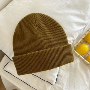 Detailed close-up of a warm olive green ribbed knit beanie on a soft bed background
