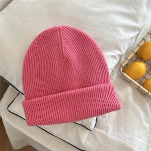 Detail of a pink ribbed knit beanie with thick cuffs on a white bedding background