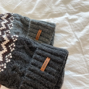 Detail of thick knit fabric with Nordic geometric pattern and brown leather brand label