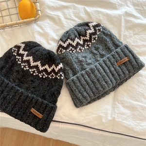 Detailed view of thick knit winter hats in grey with wave pattern and leather brand tag
