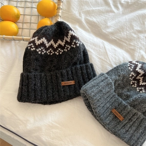 Detail of warm knitted beanie hats with wave patterns and leather labels on soft fabric