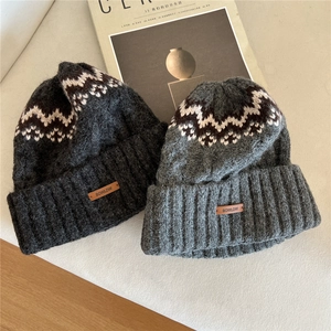 Thick Fair Isle knit beanies in grey wool with faux leather logo patch on neutral background