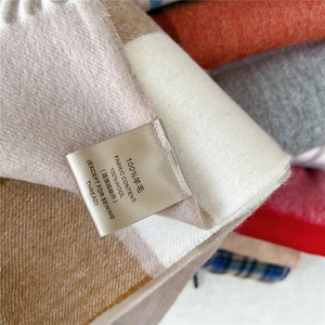 Detail of 100% wool label on a soft brown and beige plaid scarf with fringe