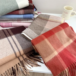 Detail view of stacked wool blend scarves featuring plaid patterns and woven fringes