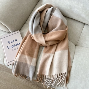 Detail of wool-touch plaid scarf with soft tassels on a grey fabric sofa surface