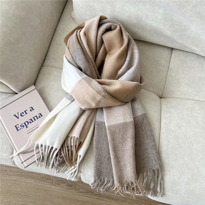 Detailed close-up of soft plaid wool scarf with fringes on beige leather sofa