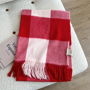 Detail of red and pink plaid wool scarf featuring fringe trim and 100% wool label