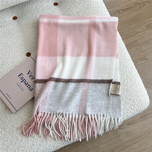 Detail of pink and grey plaid 100% wool scarf with soft fringes on a white sofa