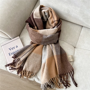 Close-up of 100% wool plaid scarf with fringes on beige sofa with decorative books