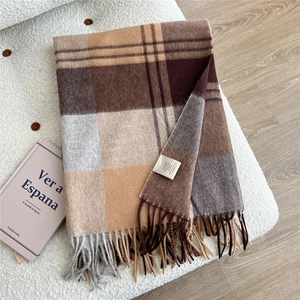 Detail of 100% wool scarf showing classic plaid pattern and fringe on a soft surface