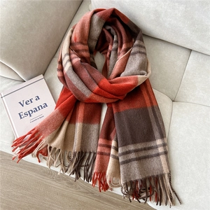 Detail of warm orange and brown plaid wool scarf with fringes on a grey sofa