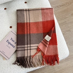 Close-up of 100% wool scarf with orange plaid pattern and soft decorative tassels