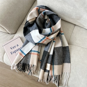 Detailed shot of a soft wool blend plaid scarf with tassels on a neutral fabric background