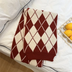 Detailed knit texture of red and white argyle scarf on a cozy bed background