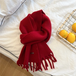 Detail of red knitted winter scarf with soft tassels and decorative metal nameplate