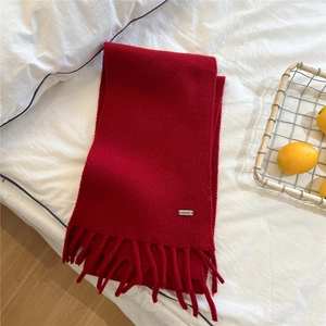 Detailed texture of a red festive knit scarf with soft tassels and brand metal tag