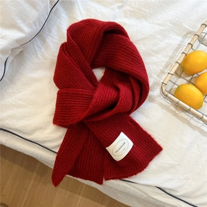 Detail of soft red knitted scarf with white brand label on minimalist fabric background