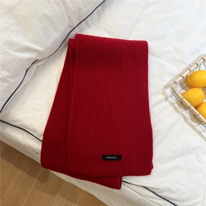 Detail of red 100% wool knitted scarf with ribbed texture on white bedding background