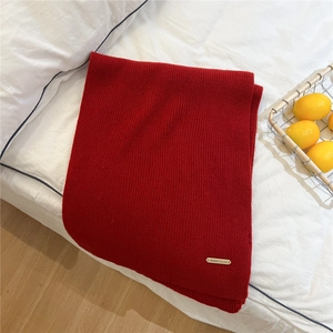 Close-up of red knit scarf texture with a golden brand label on a cozy white bed