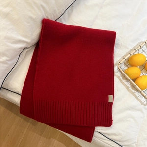 Detail of red wool knit scarf with 100% wool label and ribbed texture on white bedding