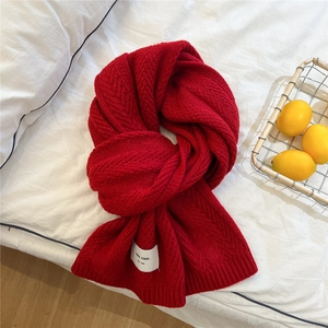 Detail shot of a thick red knitted scarf with herringbone pattern and white label
