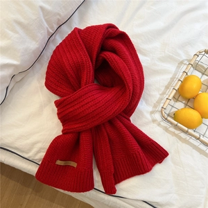 Thick red knitted scarf with ribbed texture and brand logo label on white bedding