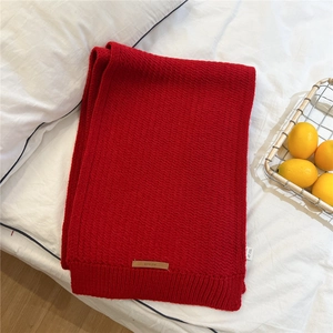 Close-up of red ribbed knit scarf with leather brand tag on white textured fabric