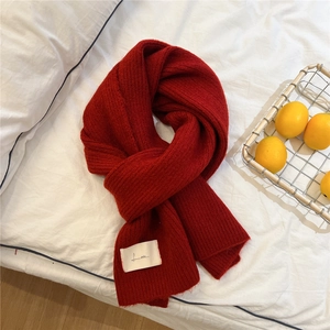 Detailed close-up of thick red knit scarf with minimalist white rectangular logo label
