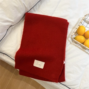 Detailed close-up of a red knitted scarf with a brand logo tag on a white bed