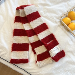 Detail of red and white striped knit scarf with stitched brand label on a cozy white bed