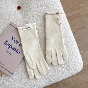 Detail of cream white knit gloves with wooden button and soft wool-like texture