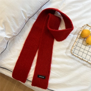 Detailed close-up of dark red ribbed knit scarf with branded woven label on white bedding