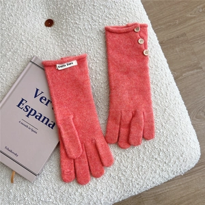Detail of coral knit gloves with wooden buttons and branded label on soft texture