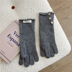 Detail of dark grey knit gloves with wooden buttons and branded label on white fleece