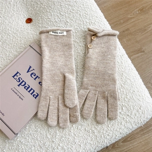 Close-up of beige knit gloves with wooden button details and brand label on soft fabric