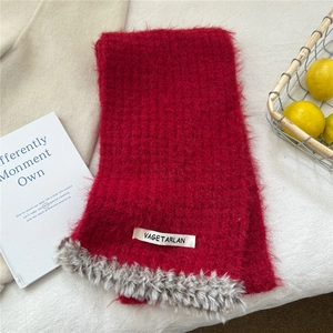 Close-up of red knit scarf with faux fur trim and brand label on white fabric