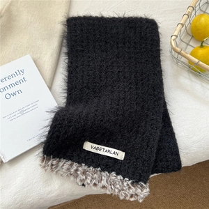 Detail of black plush scarf with faux fur trim and white woven label on fabric
