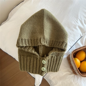 Dettaglio del passamontagna in maglia verde scuro con bottoni verde menta su lino bianco