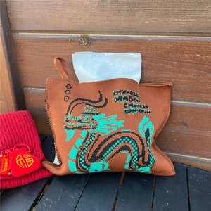 Detail of a brown knitted tissue cover featuring a green dragon pattern and hanging hook