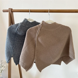 Dettaglio di poncho in maglia grigi e kaki con cerniere diagonali e trama a costine