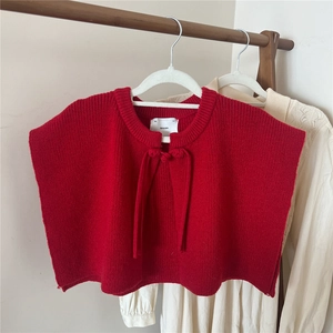 Detail of red knitted shawl vest with a round neck and matching tie-up straps