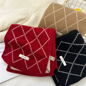 Trois écharpes en laine à losanges en rouge, camel et noir présentées sur une table