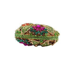 Détail de motifs floraux en cristal émeraude sur une pochette de soirée de luxe en métal doré