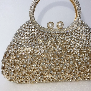 Détail de pochette dorée avec fleurs en strass, poignée en métal et fermoir perle
